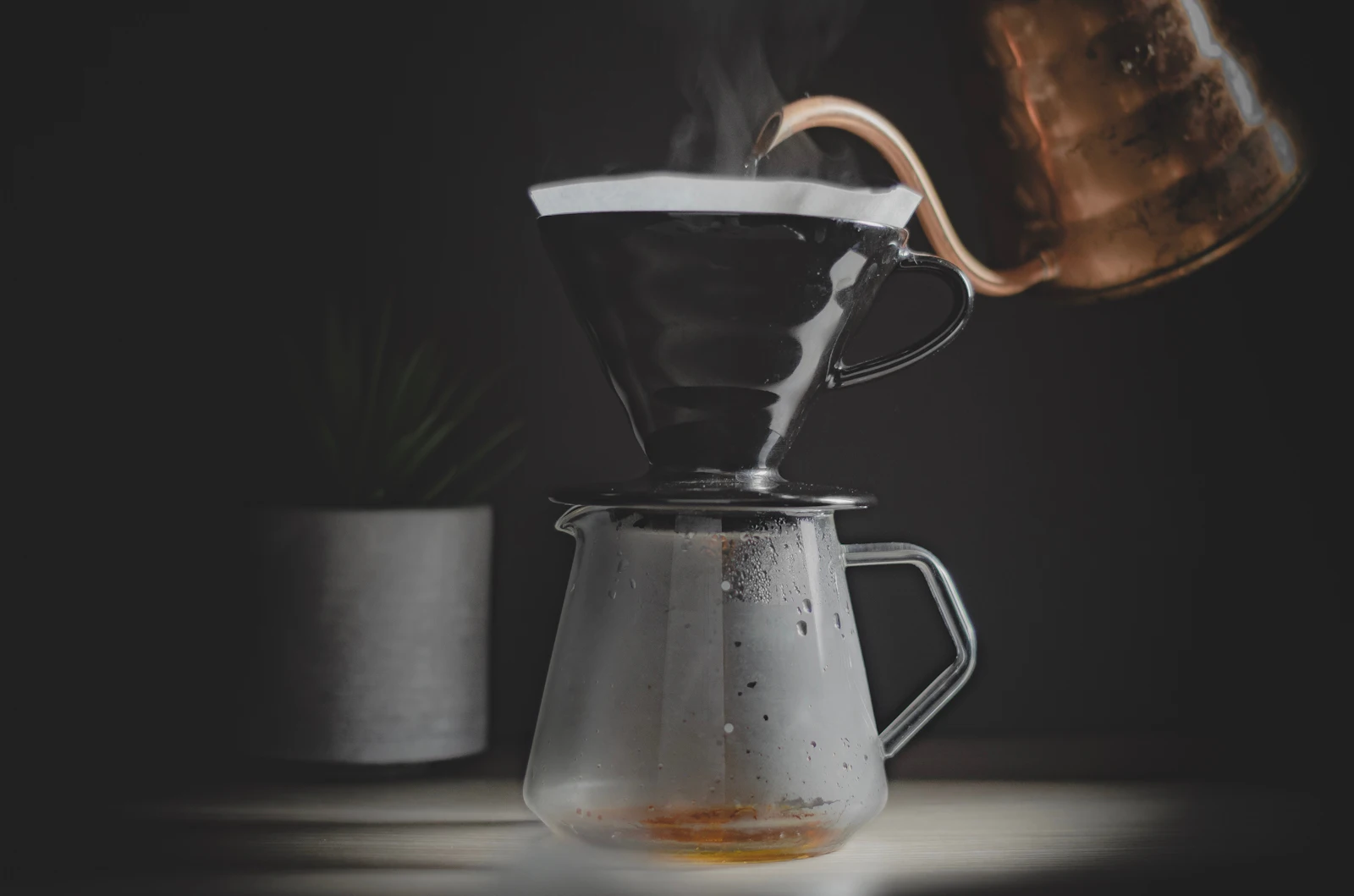 Hot water poured from a copper kettle into a pour-over dripper